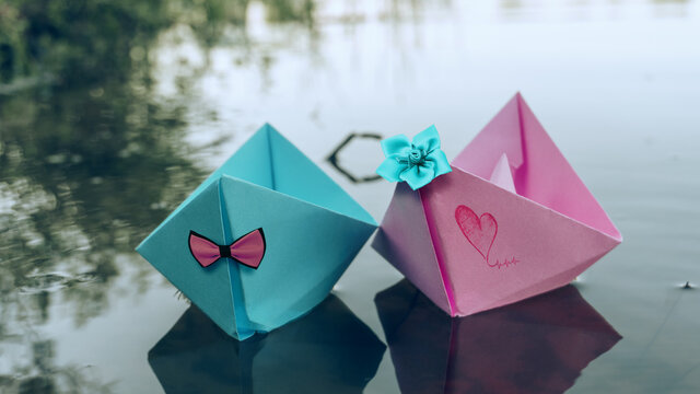 Two boats of blue and pink color, decorated with a red butterfly and a bow of green color. Paper boats float on the water. 4K