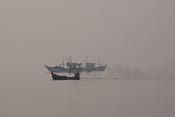 Fisherman riding boat with smoke in sea water