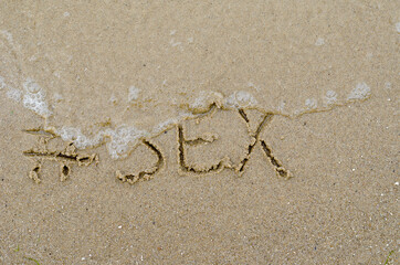 Hashtag and the word SEX written in the wet sand. The wave washe