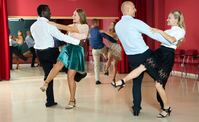 Adult dancing couples enjoying active boogie-woogie in modern studio..