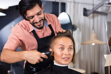 .Positive sexy adult hairdresser working with hair clipper with woman