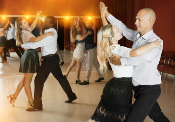 Young smiling people learning to dance waltz in dancing class..