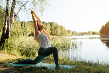 Beautiful young woman doing yoga outdoors. Fitness woman performing anjaneyasana asana on yoga mat....