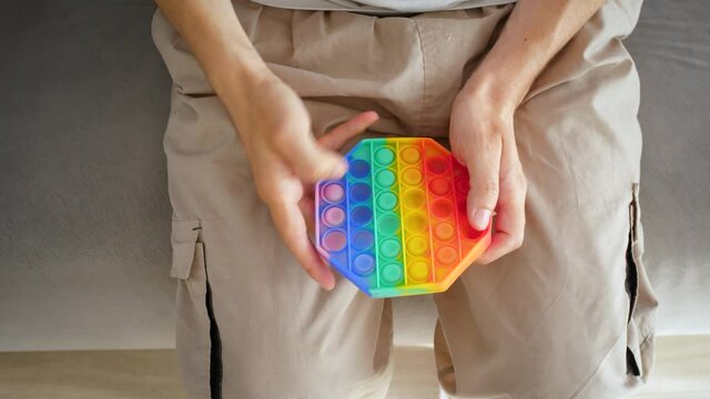 A man plays with pop it toy simple dimple in the room on the couch. the color of the rainbow. Hands close up