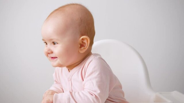 A small child boy or girl sits on a high chair and smiles. White background