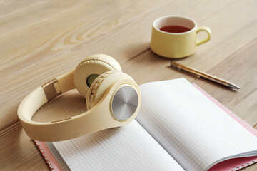 Modern headphones, cup of coffee and notebook on wooden table, closeup