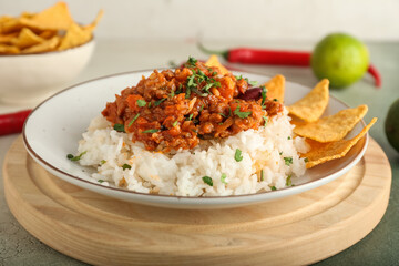 Plate with tasty chili con carne, rice, lime and nachos on color background, closeup