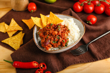 Bowl with tasty chili con carne, rice, nachos and vegetables on wooden background