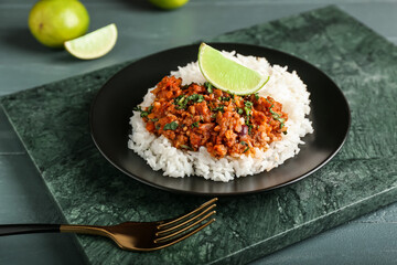 Plate with tasty chili con carne, rice and lime on color wooden background