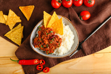 Bowl with tasty chili con carne, rice, nachos and vegetables on wooden background
