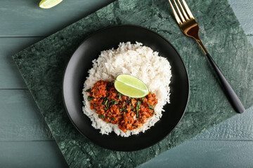 Plate with tasty chili con carne, rice and lime on color wooden background