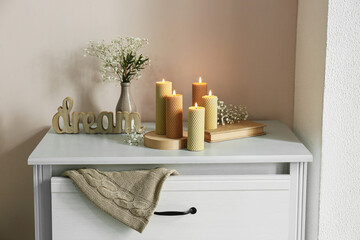Burning candles and vase with flowers on chest of drawers in room