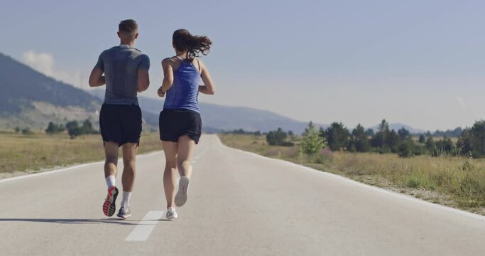Tracking slow motion shot of sportive couple jogging outdoors in the morning, trail running experience in nature. Healthy lifestyle concept.