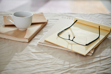 Notepads and planners on bed of student as well as glasses and cup of coffee