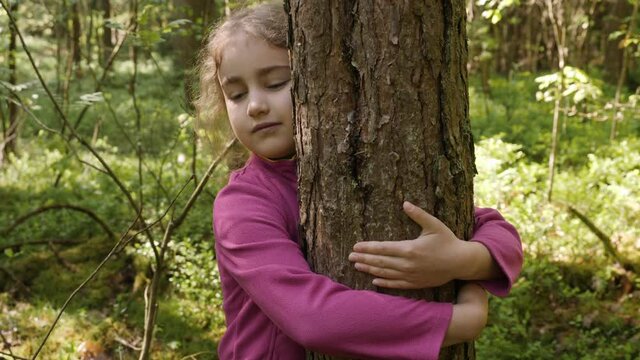 Contented Little Girl Hugging Large Tree With Blissful Expression of Nature Conservation. Harmony Calm Relaxation. Save Earth Green Planet. Child Girl Hugging Tree Trunk in Park, Nature Life Love.