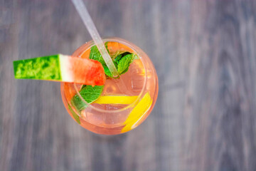 Pink mojito cocktail with mint, lemon slices and ice on a wooden table. Decorated with a slice of...