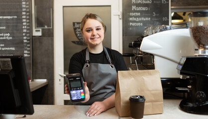 Caucasian barista with a payment terminal for contactless payment with nfs in a cafe prepared an...