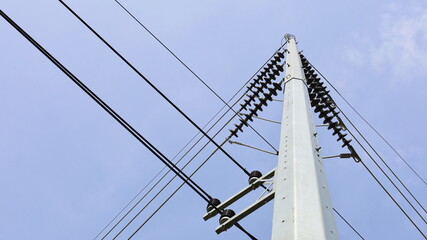 Insulated with high voltage wires on metal poles. Steel poles support high and low voltage transmission lines in urban area in bottom view on blue sky background with copy space. Selective focus
