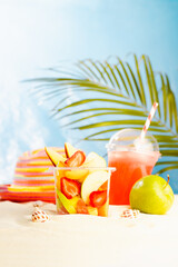 Resort lifestyle - picnic with cold cocktail, fresh tropical fruit salad, sun hat on white sand with palm, sun glare in blue sea view, vertical. Vacation on ocean beach.