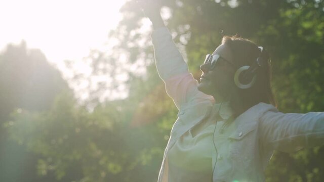 Beautiful woman wearing headphones listen music and dancing in park in early summer morning outside