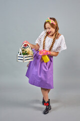 Young beautiful farmer woman wearing apron and hair braids with plants. Full-size portrait of girl holding fresh plants on gray background. Pin up style.