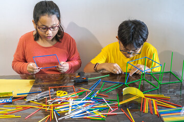 Young children are constructing colorful plastic sticks with glue gun. fun with building geometric figures and learning mathematics at home.