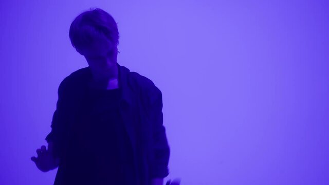 Talented man dancing hip hop or vogue on purple neon background in studio. Shooting of modern choreography with hand movements, guy dancer expressing feelings for music video performance. 