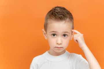 Little boy points a finger to his head isolated on an orange background. Concept of great idea or thought, good memory. 
