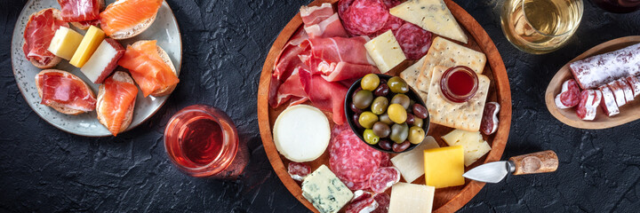 Italian antipasti or Spanish tapas panorama on a black background. Gourmet cold meat and cheese...