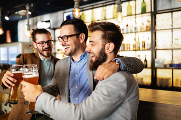 Leisure, friendship pub concept. Happy male friends drinking beer and clinking glasses at bar or pub