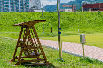 Wooden swing park bench beside walkway with city buildings in background.