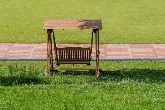 Rear view of wooden swing park bench beside walkway.