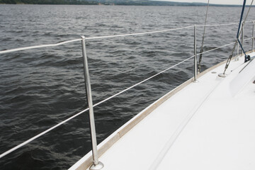 Obraz premium Boat trip on the river. Details about the sailing yacht. In the summer, we go by boat. A white yacht with full sails. Leisure, sports, recreation theme. Close-up view of the metal railing.