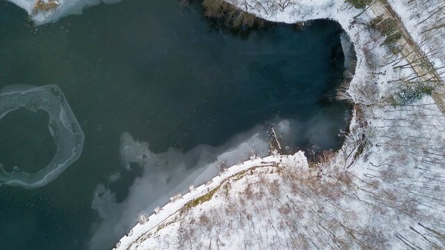 Aerial view of the winter snow covered forest and frozen lake from above captured with a drone. High quality photo