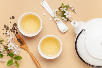 Spring tea ceremony. Herbal tea in cups, teapot and branches of blossoming cherries. Top view. Flat...