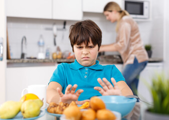 Portrait of school age boy sitting at kitchen table do not want to eat
