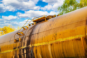 A close-up of an old railroad tank car with drips on board. A freight train is temporarily parked...