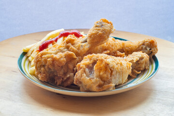 Plate with several fried chicken leg and fries on a wooden background. Side view