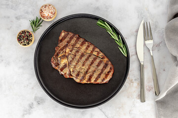 Traditional entrecote, cut from the rib. Medium rib eye steak on the plate with cutlery and seasonings.