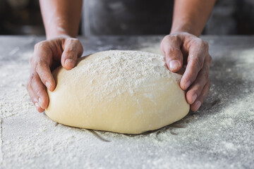 The chef is kneading the dough to make fresh bread on the kitchen table.
