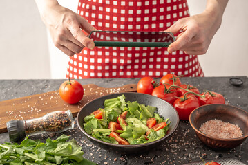 Women's hands are holding a mobile phone over a beautiful appetizing vegetable salad to take a photo