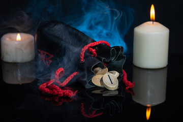 Rune Isa associated with an ice block, immobility. The rune fell out of an antique leather bag against the background of candles and blue smoke with the reflection of the rune. Selective Focus