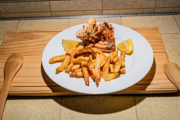 Homemade grilled chicken served on a ceramic white plate with with rustic fried potatoes and sauce. Isolated over wooden board.