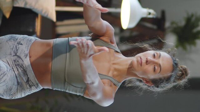 Vertical format video of young attractive woman in sportswear performing warrior pose while practicing yoga at home