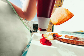 point of view from the plate of a child pressing the ketchup bottle pouring tomato sauce near sausage and potatoes and carrots - fisheye saturated outdoor shoot