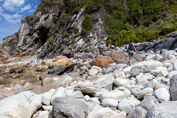 people walking on a hiking trail over big boulders at the coast