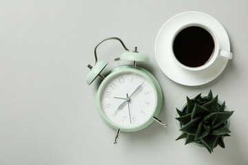 Alarm clock, coffee and succulent on light gray background