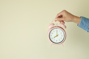 Female hand holds alarm clock on beige background