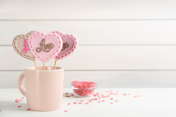 Heart shaped lollipops made of chocolate in cup and sprinkles on white table, space for text