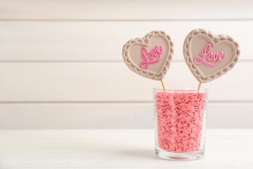 Heart shaped lollipops made of chocolate with sprinkles in cup on white table, space for text
